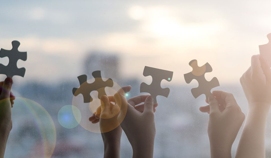 Hands holding puzzle pieces against bright sky symbolizing teamwork and collaboration